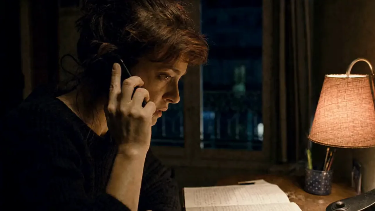 A woman answers a late-night call at her desk, lamp on, notebook open